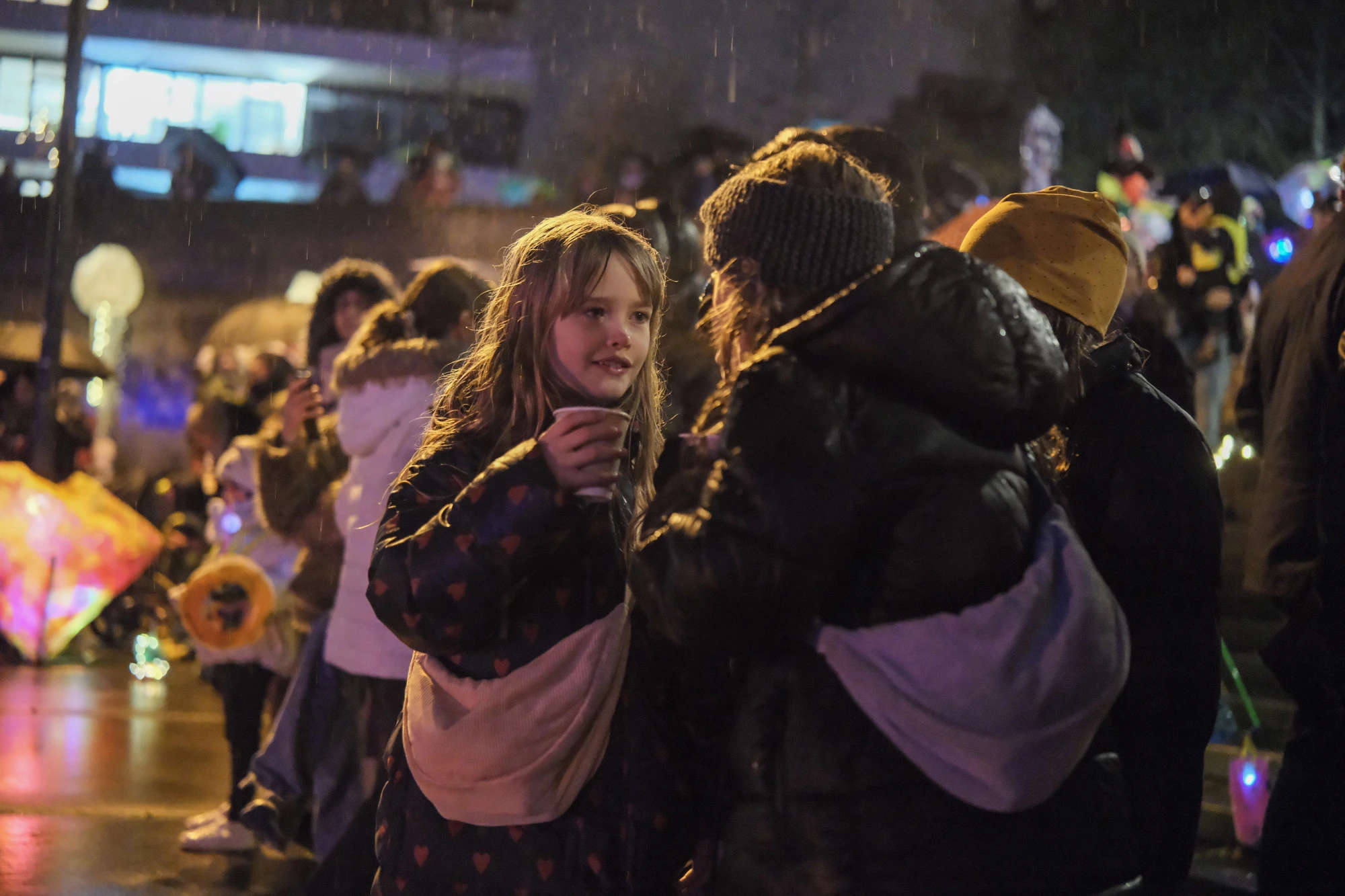 Gruppe von Menschen bei Nacht, einige tragen Winterjacken und Mützen, im Hintergrund bunte Lichter und ein gelbes Zelt.