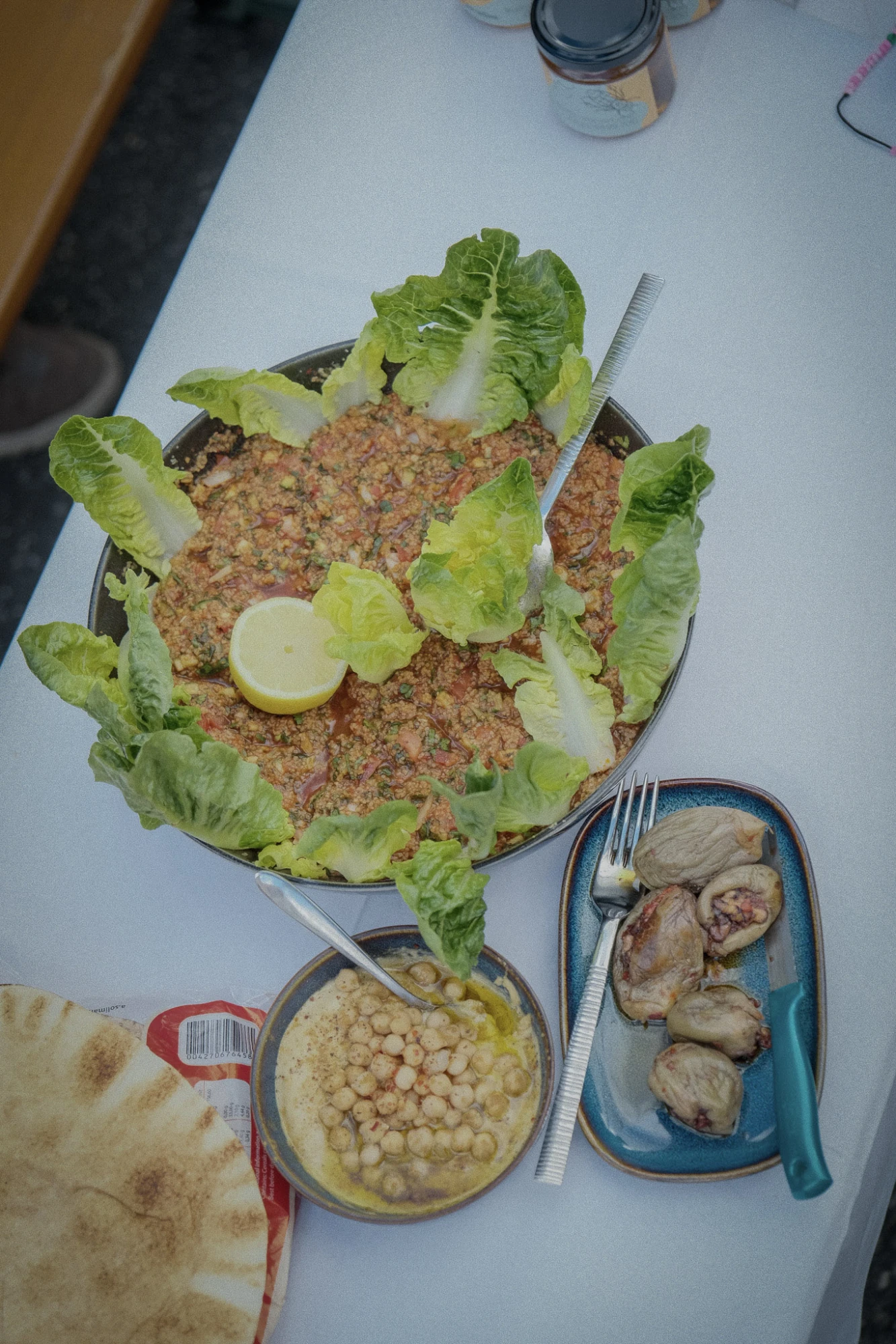 Mehrere Schalen mit Essen. Es sieht aus wie Couscous Salat. Außerdem frishce Salatblätter, Zitrone, etwas Fladenbrot und Kichererbsen.