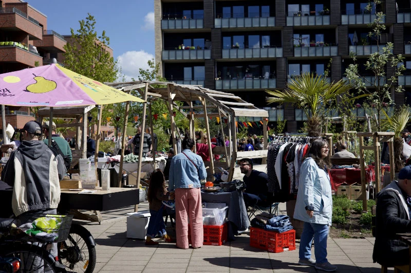 Marktstände mit Kleidung und anderen Waren in einem belebten Innenhof mit mehreren Personen und Wohngebäuden im Hintergrund