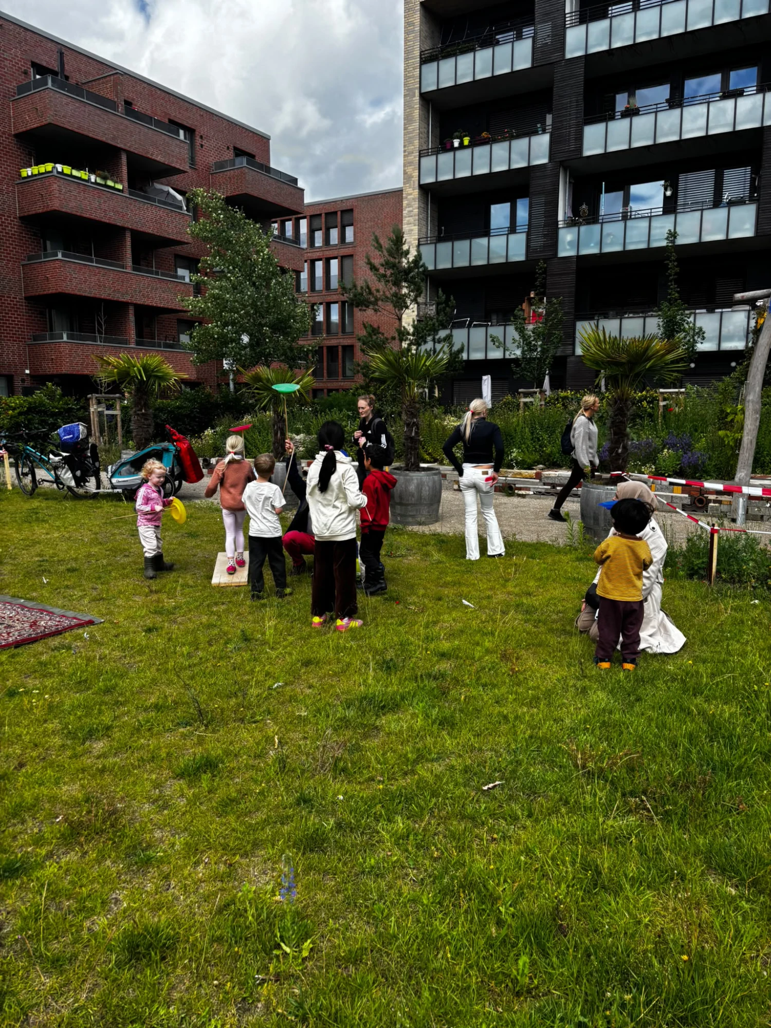 Kinder spielen auf einer Wiese vor modernen Wohngebäuden unter bewölktem Himmel