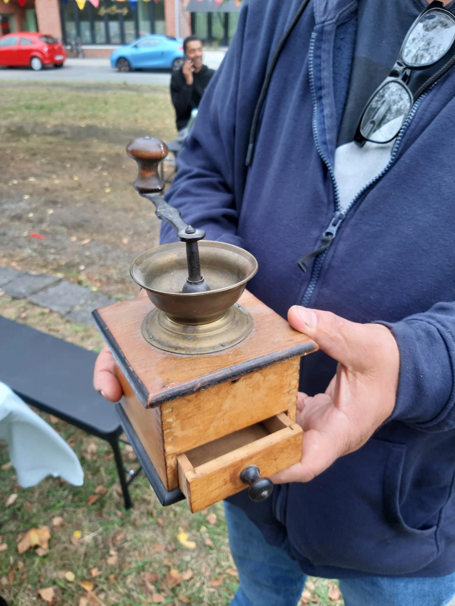 Person hält eine antike manuelle Kaffeemühle aus Holz mit Metallkurbel und offenem Schubladenfach