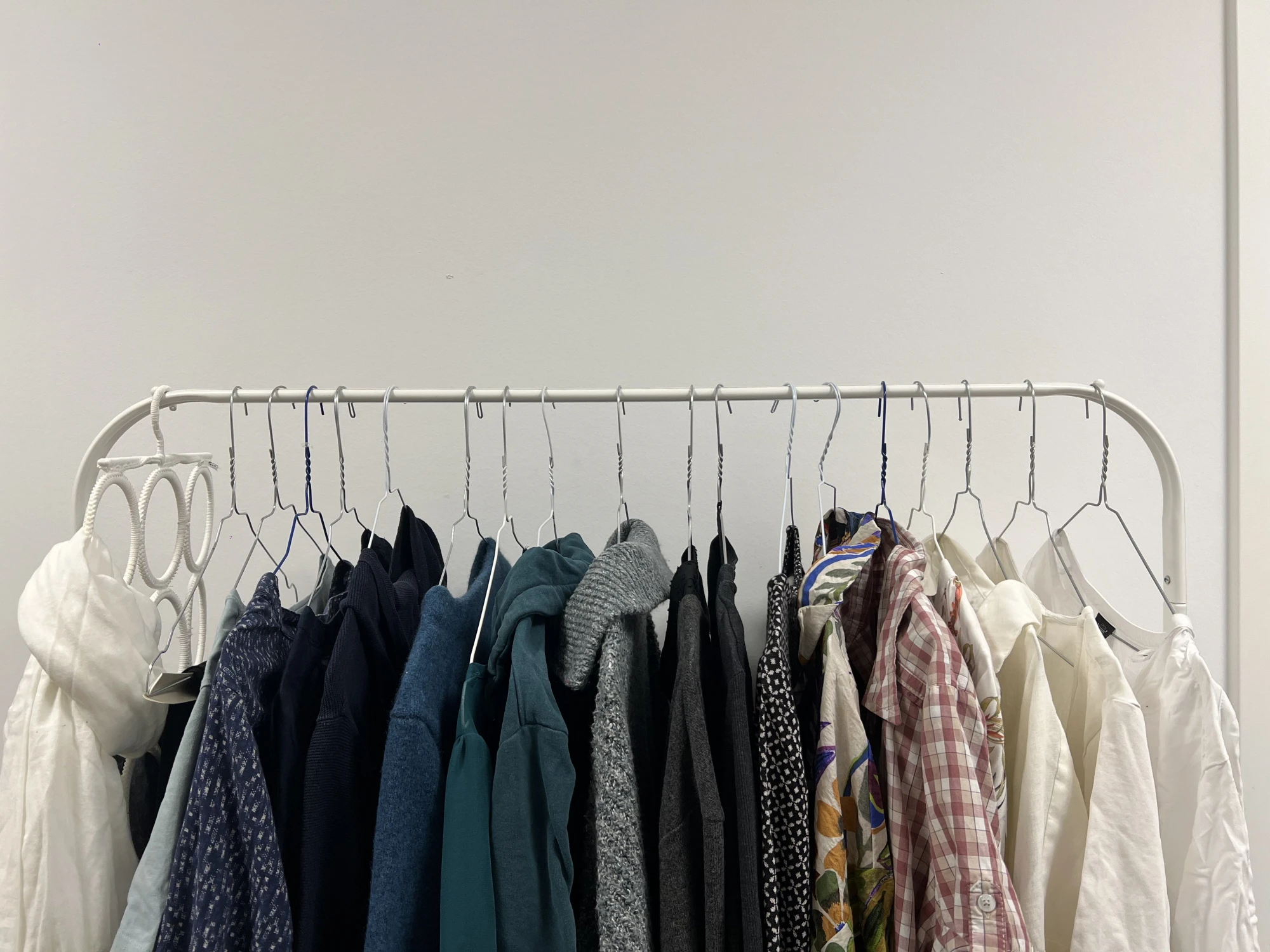 Kleiderstange mit mehreren Jacken, Hemden und einem weißen Schal, die auf Kleiderbügeln hängen