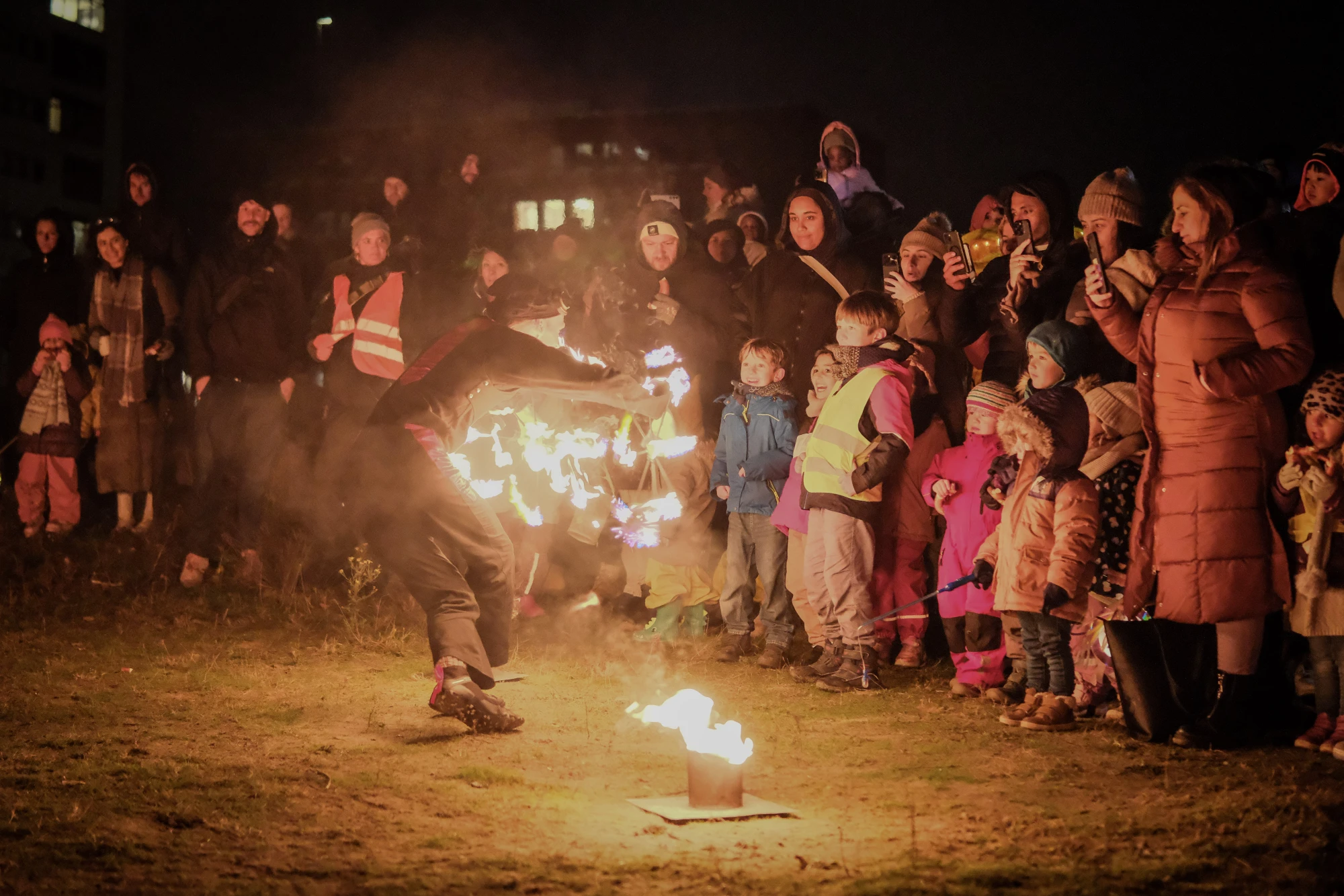 Ein Feuerkünstler schwingt Feuerstäbe. Rund herum stheen viele Kinder und auch Erwachsene. Einige weichen nach hinten, weil das Feuer ihnen so nah kommt.