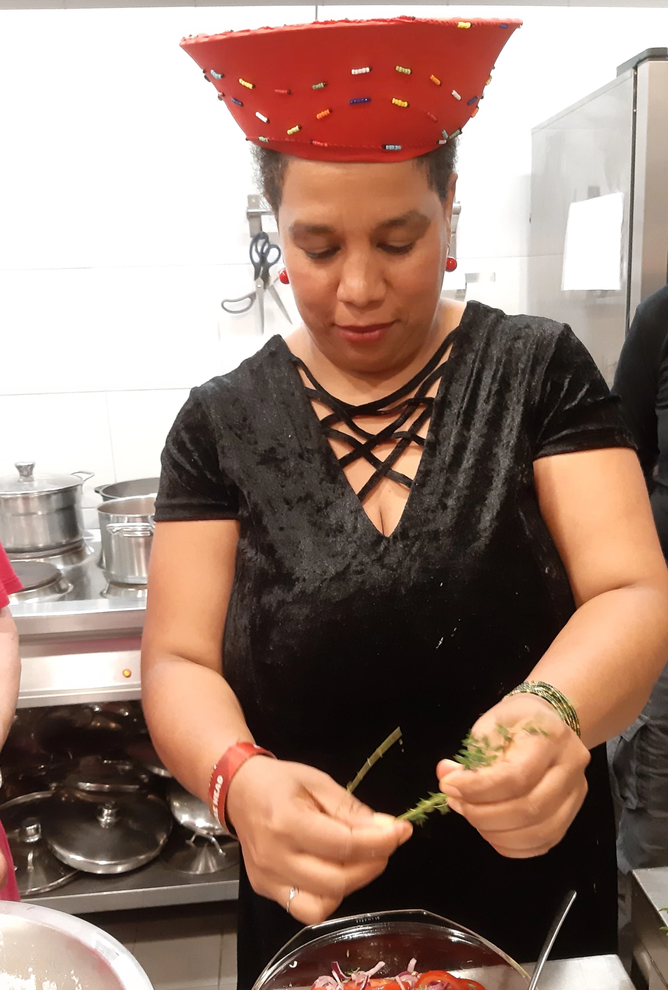 Eine Frau im schwarzen Kleid mit rotem Hut bereitet einen Tomatensalat zu.
