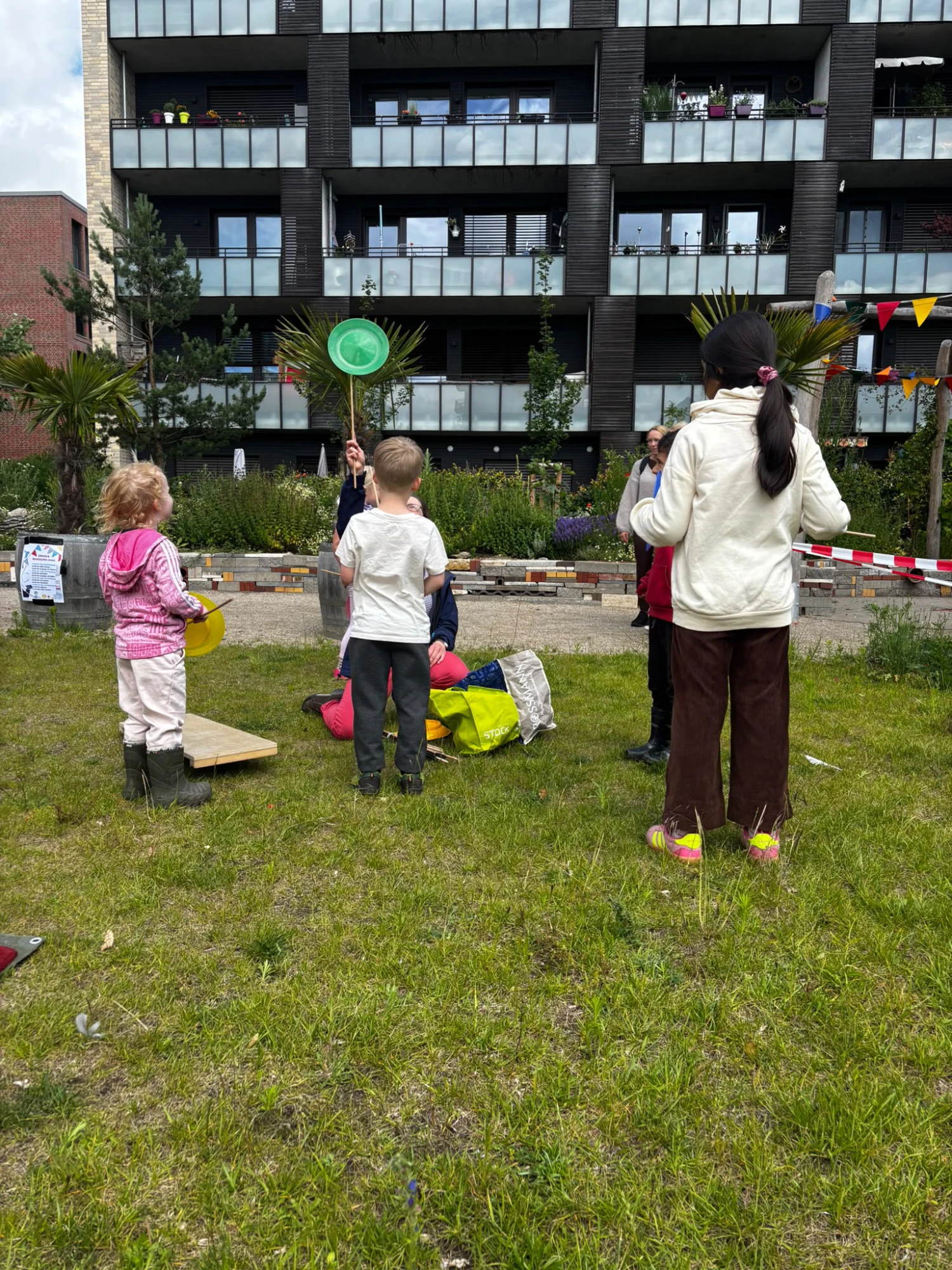 Mehrere Kinder stehen auf einer Wiese vor einem Wohnhaus und spielen mit bunten Tellern