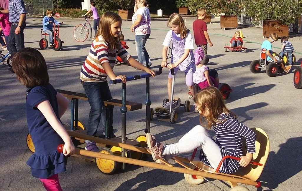 Kinder spielen auf einem Hof mit verschiedenen Tretfahrzeugen und Holzspielzeugen