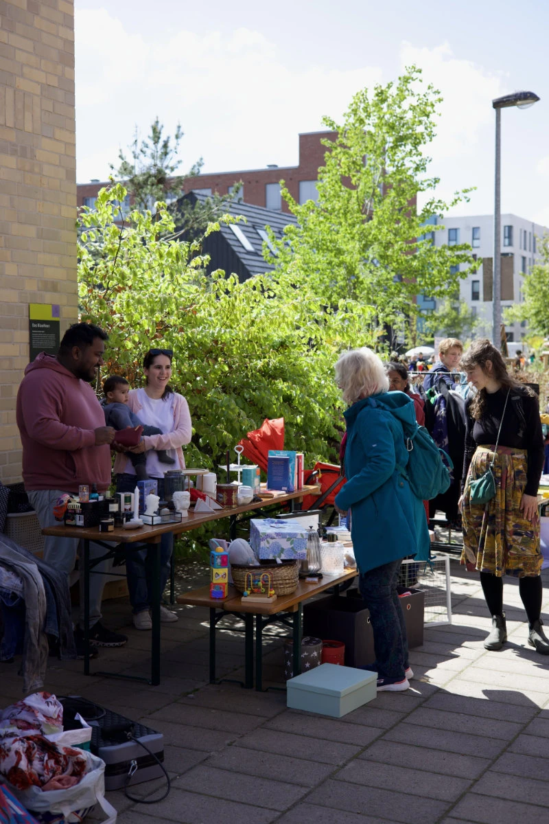Mehrere Personen stehen an einem Tisch mit verschiedenen Gegenständen im Freien vor einem Gebäude