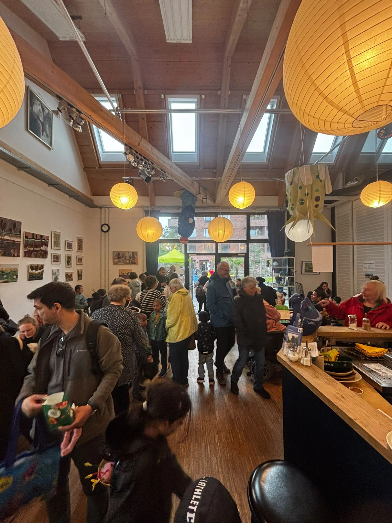 Innenraum eines Cafés mit vielen Menschen, hängenden runden Lampen und Holzbalkendecke