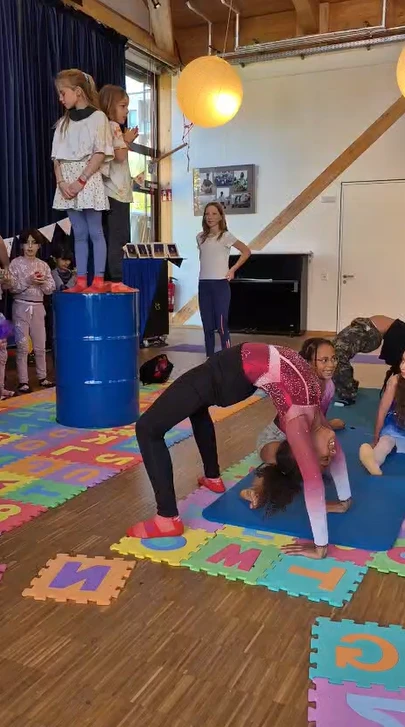Kinder führen Akrobatikübungen in einem Raum mit bunten Schaumstoffbuchstabenmatten durch